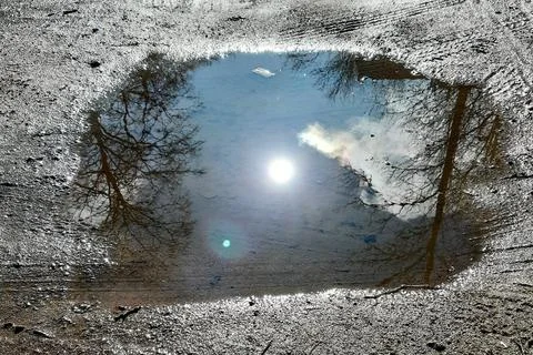 Puddle on the ground with a reflection of the blue sky and the bright sun. Stock-Fotos