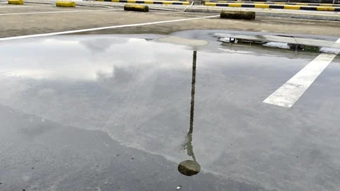 A puddle in a parking lot reflecting off a lamppost in a cloudy sky Stock Footage 304617682
