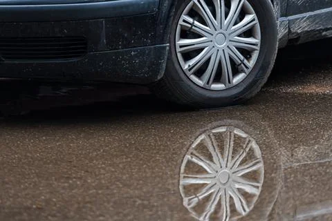 Puddle on the pavement with a reflection of the car wheel, closeup Stock Photos