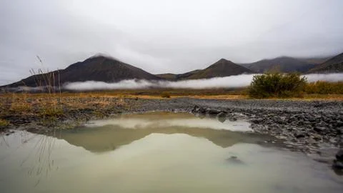 Puddle of rain with reflection in the front. Mountain with fog in the backg.. Foto stock