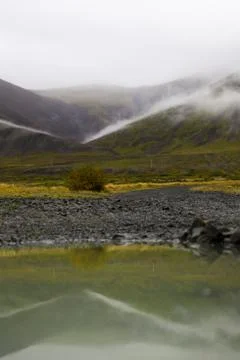Puddle of rain with reflection in the front. Mountain with fog in the backg.. Stock Photos