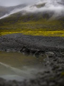 Puddle of rain with reflection in the front. Mountain with fog in the backg.. Stock Photos