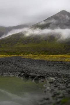 Puddle of rain with reflection in the front. Mountain with fog in the backg.. Stock Photos
