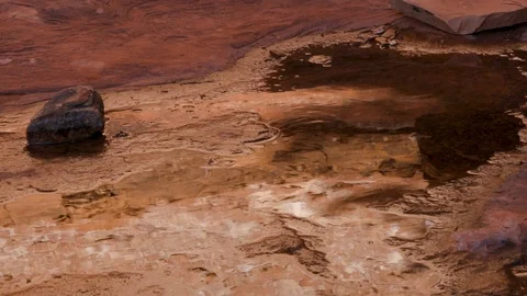 A puddle in a red rock canyon splashes as a shoe walks through the puddle. Stock Footage 124494336