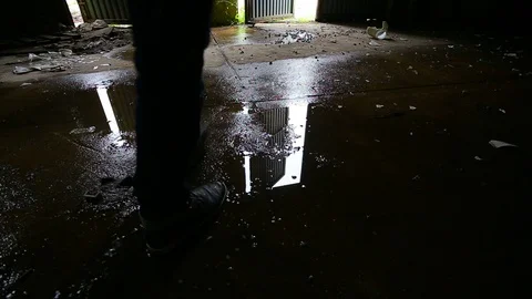 Puddle reflection of a man leaving dark abandoned building. Video footage. Stock Footage 107651214