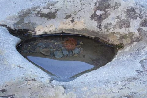 Puddle in a rock with pebbles and a leaf submerged Stock Photos
