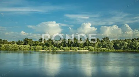 The puffy clouds above forest and river (lake) Stock Photos