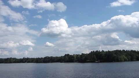 Puffy clouds over a lake flow by in this timelapse. Video stock 73607097