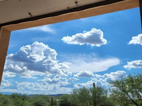 Puffy cumulus clouds in blue sky seen from inside garage Stock Photos