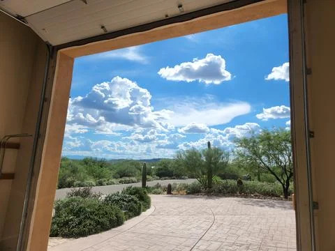 Puffy cumulus clouds in blue sky seen from inside garage Stock Photos