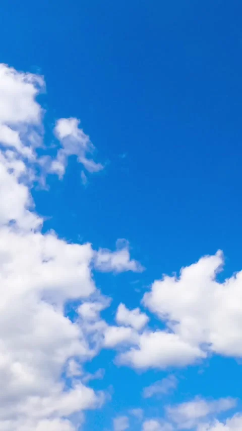 Puffy white clouds drift across a vibrant blue sky in a vertical time lapse.. Stock Footage 337538643