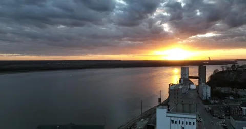 Pull back flight viewing a sunset and clouds over river and commerce along river Stock Footage 335669414