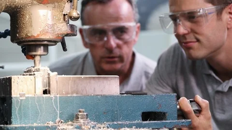 Pull Focus Shot Of Engineer Training Male Apprentice To Use Drill In Factory Video stock 93376897