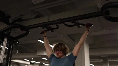 Pull-ups on a sturdy bar. A young man with curly hair and glasses performs the e Stock Footage 301677350