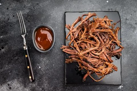Pulled beef brisket on black slate board, dried smoked meat snack, protein .. Stock Photos
