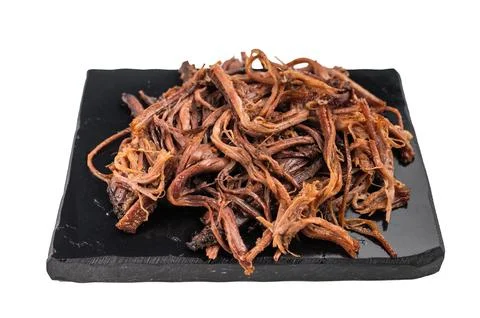 Pulled beef brisket jerky on black serving plate, dried meat snack close up.. Stock Photos