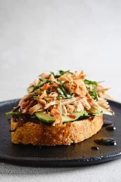 Pulled pork toast topped with caramelized onions and fresh herbs served on .. Stock Photos