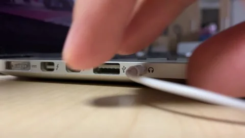 Pulling 3.5 mm audio cable from port socket notebook on wooden desk close up Stock Footage 250446773