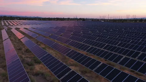 Pulling back wide view of solar farm and panels with sunset and power lines Stock Footage 160889674