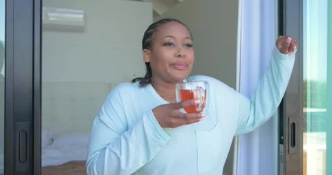 Pulling curtain at bedroom door, African American woman sipping tea from glass Stock Footage 342392311