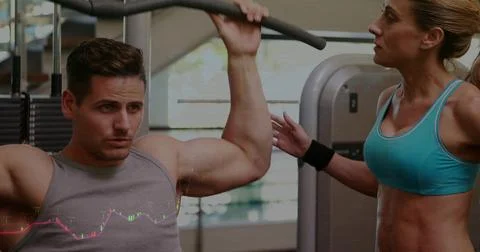 Pulling lat pulldown, trainee in gray tank, trainer in turquoise top guiding at 스톡 사진