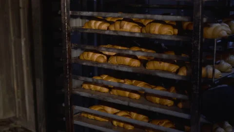 Pulling out a rack of plates with croissants during working process in a bakery Video stock 147256061