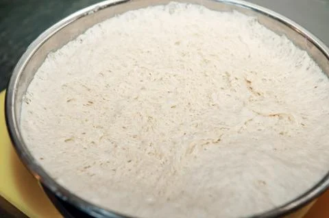 Pulling the plastic wrap off the raised bread dough in a metal mixing bowl. T Stock Photos