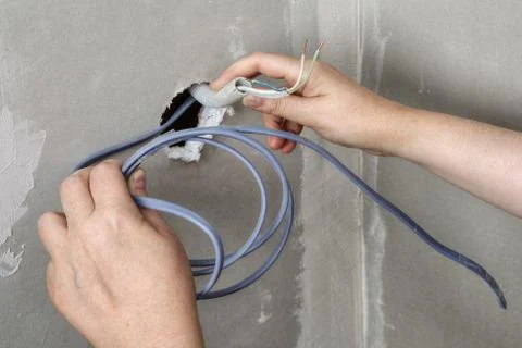 Pulling wires through wall hole, electrician hands close-up. 写真素材