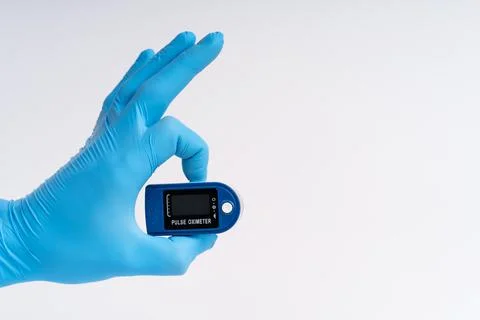 Pulse oximeter on a white background. A hand in a medical glove holds a devic Stock Photos