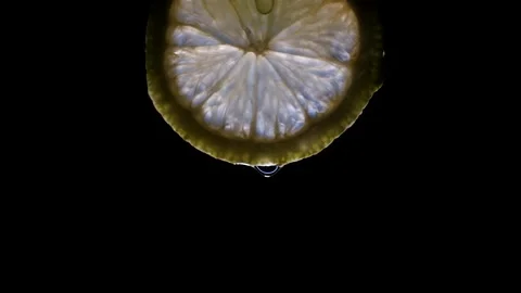 A pulsing light lights up a lemon slice isolated on a black background. Video stock 143502332