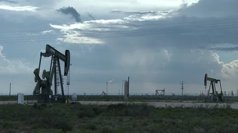 Pump jacks against dramatic sky as gas is flared off in b.g., 4K. Stock Footage 79978020