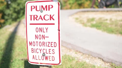 Pump track sign along empty curving path early morning sunlight casting long Vídeo Stock 323979623