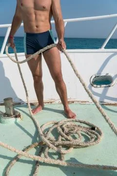 The pumped guy holds the rope on the bow of the yacht Stock Photos
