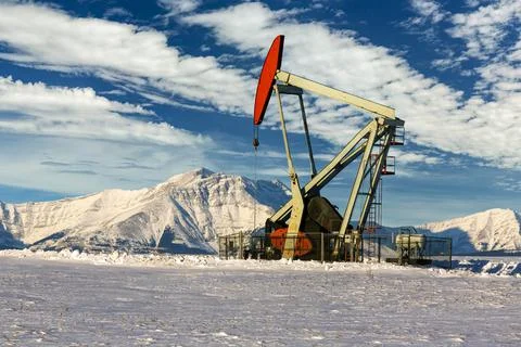 Pumpjack in a snow-covered field with dramatic clouds in a blue sky with snow-co Stock Photos
