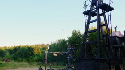 Pumpjack tower stands by wellhead as wind turbine rotates Video stock 323886673