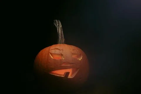 Pumpkin with face carved into a jack o lantern on black background with smoke Stock Photos