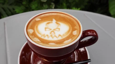 Pumpkin ghost latte art on coffee cup vibrating slightly for spooky holiday vibe Stock Footage 343945280