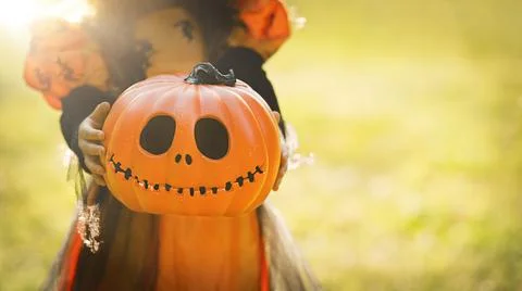 Pumpkin head Jack-o'-lantern in the hands of a girl in a witch costume on the Stock Photos