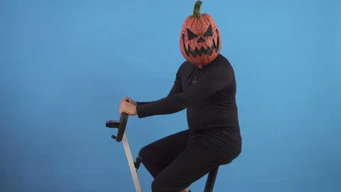 Pumpkin headed man on an exercise bike on a blue background Video stock 141604015
