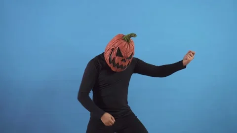 Pumpkin headed man with a scary face on a blue background plays an imaginary Stock Footage 141672696