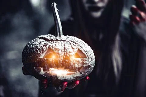 Pumpkin lantern in witch hand. Old woman holding pumpkin in dark forest. Ha.. Stock Photos