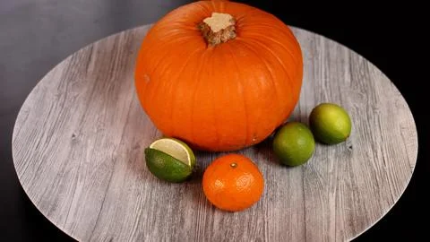 Pumpkin, limes, orange on rustic surface evoke seasonal Halloween spirit. Warm Stock Photos