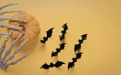 Pumpkin with plastic skeleton hand and flying bats on yellow Stock Photos