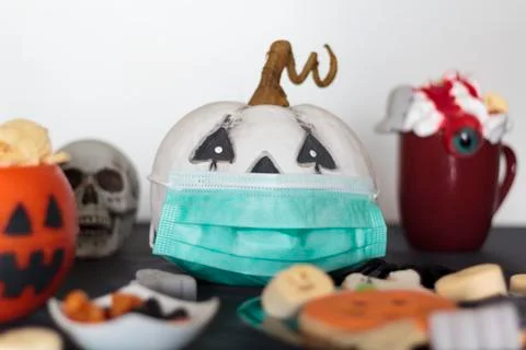 Pumpkin with protective face mask on table with treats and snacks. Celebratin Foto stock