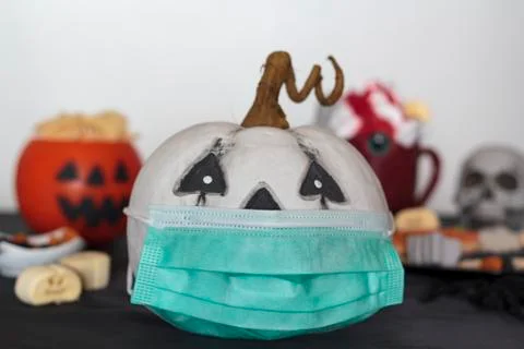 Pumpkin with protective face mask on table with treats and snacks. Celebratin Stock Photos
