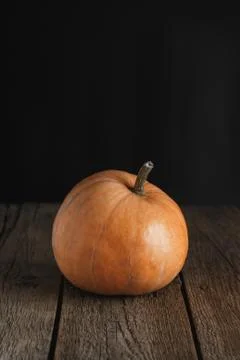 Pumpkin on a rustic wood table on dark background. Front view. Copy space. Stock Photos