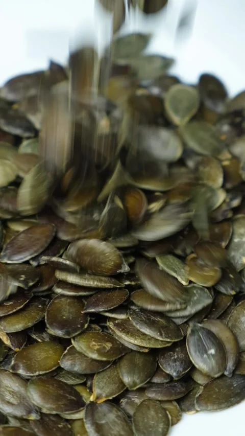 Pumpkin seed kernels pouring into the plate, vertical slow motion. Video stock 277690357