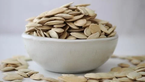 Pumpkin seeds in a bowl on a white surface Stock Footage 344234772