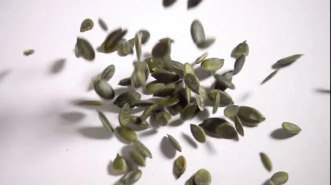 Pumpkin seeds falling in slow motion onto white table Stock Footage 55452925