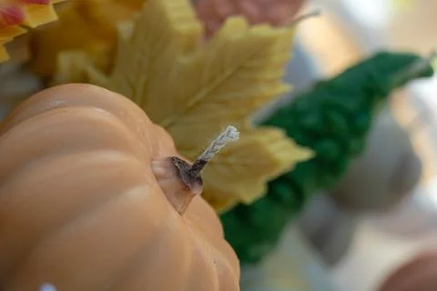Pumpkin shaped candle with visible wick and autumn leaf decorations in warm.. Stock Photos